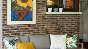 A cozy living room with a brick wall, a framed painting, a wooden sofa with cushions, a round wooden coffee table with fruit, and a window with a clock. - Oroimena Landetxea, house with swimming pool in Leitzaran, 15 min from San Sebastian. (Andoain)