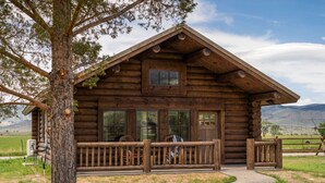 A log cabin with a porch, large windows, and a view of mountains in the background. - Beautiful Log Cabin Near Fishing Access To Yellowstone (Livingston)