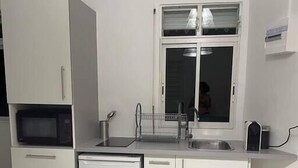 A compact kitchen with white cabinets, a built-in microwave, a sink, and a window above it. - Love Nest in the heart of the forest (Petit Bourg)
