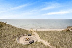 Eine Terrasse direkt am Strand mit Feuerstelle, Sitzgelegenheiten und einem Holzdeck, das zum Strand führt.