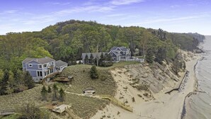 A coastal property with multiple houses, a sandy beach, and a forested hill. - Custom Lake Michigan Beachfront Vacation Home (Manistee)