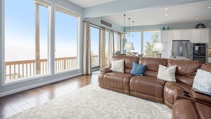 A spacious living room with a brown leather sofa, large windows, and a view of the beach. - Custom Lake Michigan Beachfront Vacation Home (Manistee)