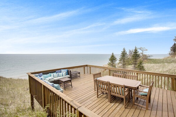 A wooden deck with a table and chairs, overlooking a body of water and surrounded by trees.