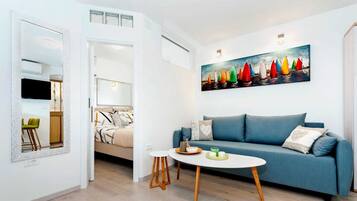 Un salon moderne avec un canapé bleu, une petite table ronde et un tableau représentant des voiliers aux couleurs vives.