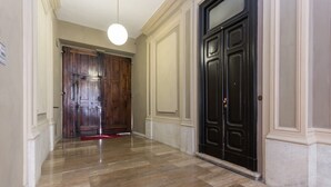 A hallway with a polished stone floor, a wooden door, and a black door with a glass panel.