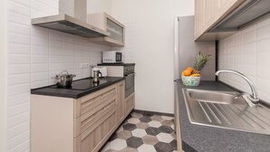 A compact kitchen with white tiled walls, a black countertop, and a stainless steel sink.