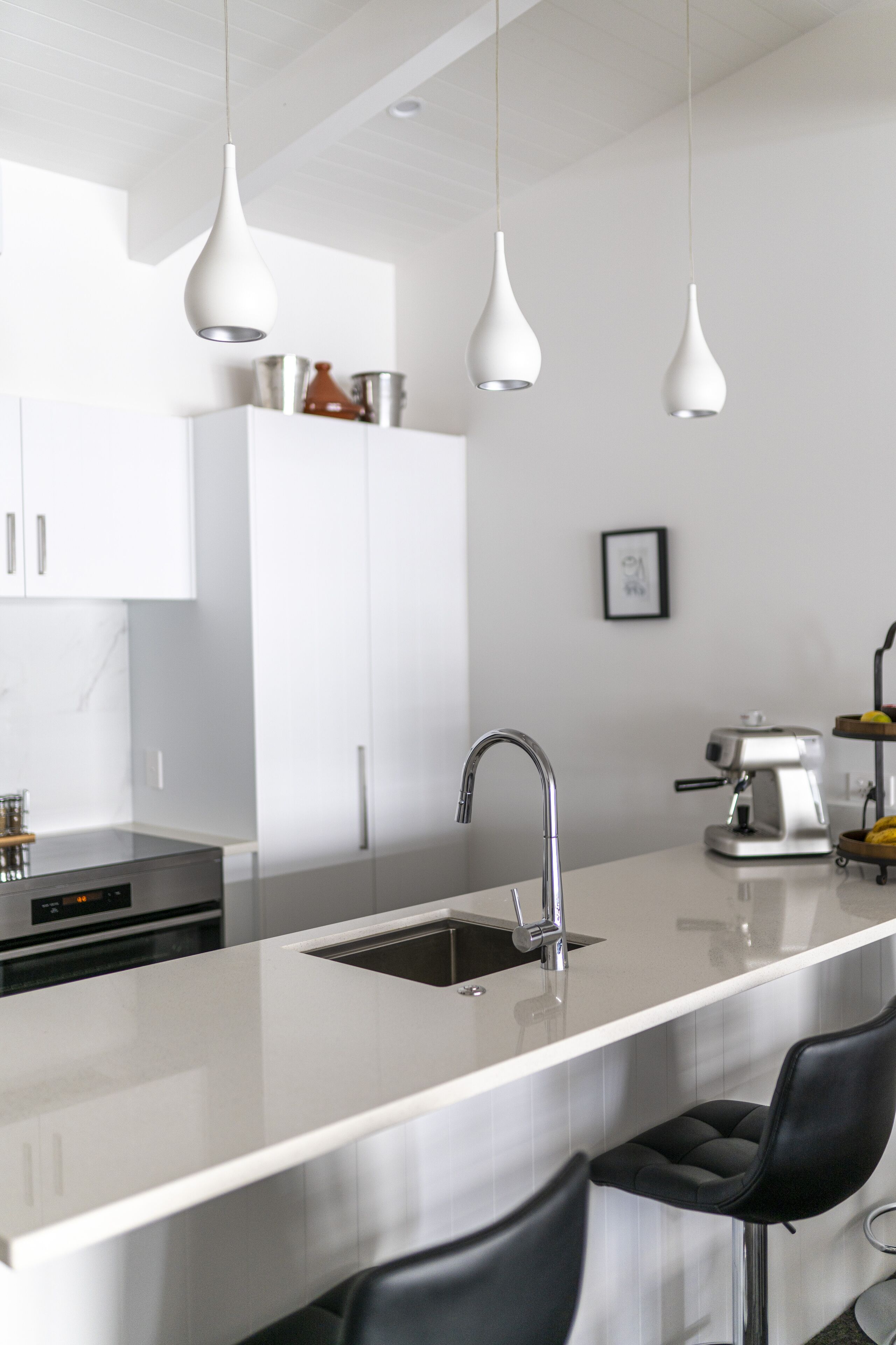 A modern kitchen with white cabinets, a stainless steel sink, and pendant lighting.