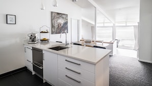 A modern kitchen with a central island, built-in appliances, and a large window providing natural light. - Whale Bay Surf House + Spa - Absolute Waterfront (Waikato)