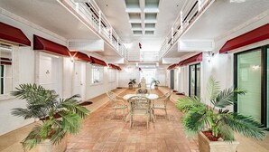Un pasillo interior amplio con una zona de estar central, plantas en macetas y un techo alto con tragaluces.