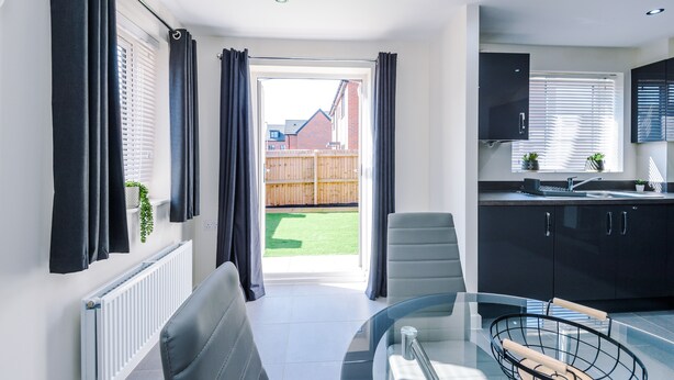 A modern kitchen with dark cabinets, a glass dining table, and a view of a backyard. - 3 Bedroom House with River Irwell view, sleeps 6 (Salford)