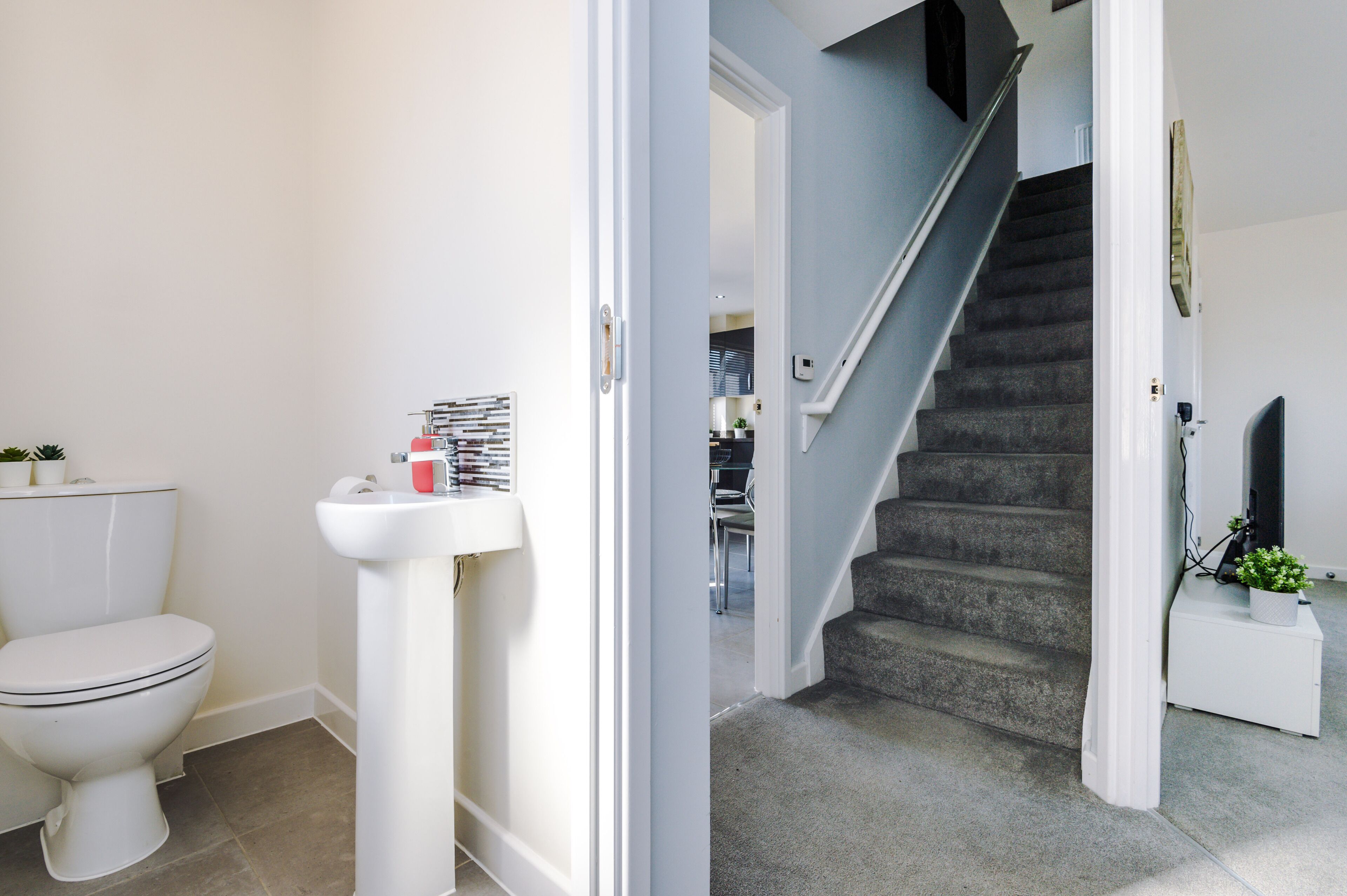 A bathroom with a toilet, sink, and a staircase leading to another room.