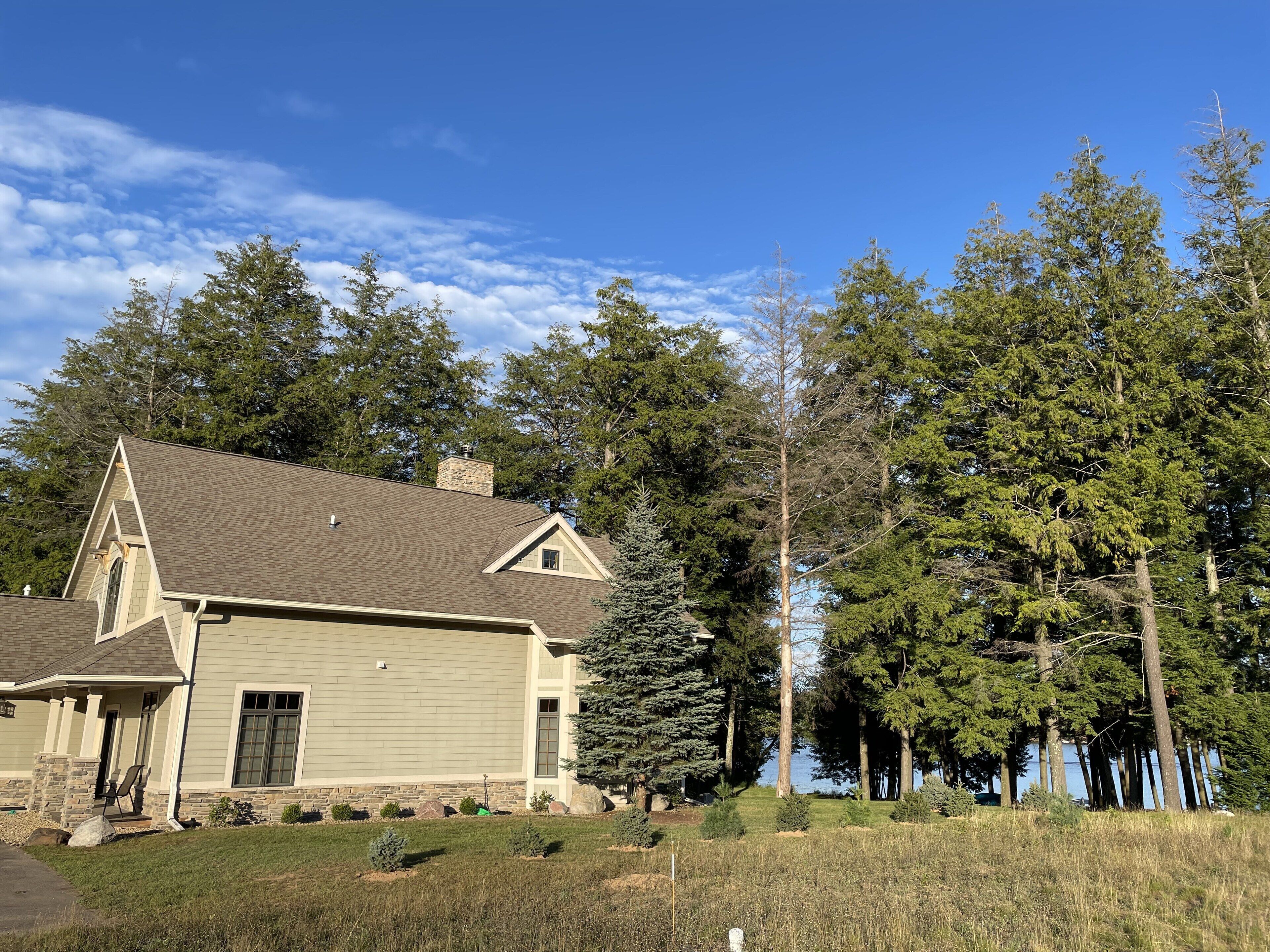 A single-story house with a gabled roof, a stone chimney, and a front porch with a chair.