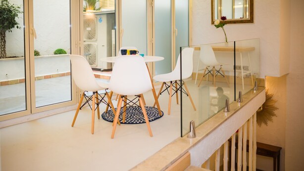 Un comedor moderno con sillas blancas y una mesa redonda, una barandilla de vidrio y vistas al exterior.