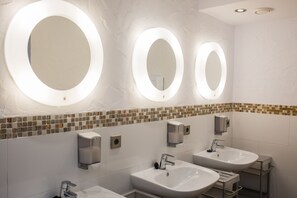 Un baño moderno con tres lavamanos, un espejo y un dispensador de jabón.