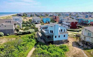 Houses with modern and traditional designs sit amidst lush greenery and a nearby beach.