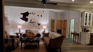 Ein Wohnzimmer mit Kuhfellwand, Deckenventilator, Kamin und Küchenzeile mit Schränken.