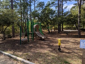Explore the playground area, featuring a slide and climbing structures surrounded by trees and a nearby bench.