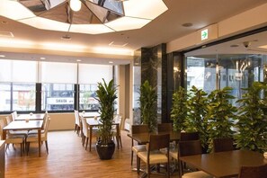 A modern dining area with wooden tables and chairs, potted plants, and large windows offering a view of the outside. - Rhino (Kyoto)