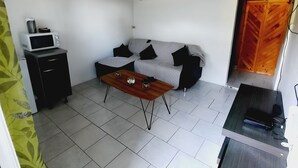 En kompakt opholdsstue med sofa, sofabord, mikroovn på et lille skab og træloft.