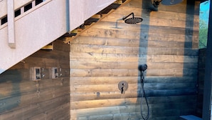 Een houten hut met een inpandige douche, inclusief een handdouche en een douchekop aan de muur.