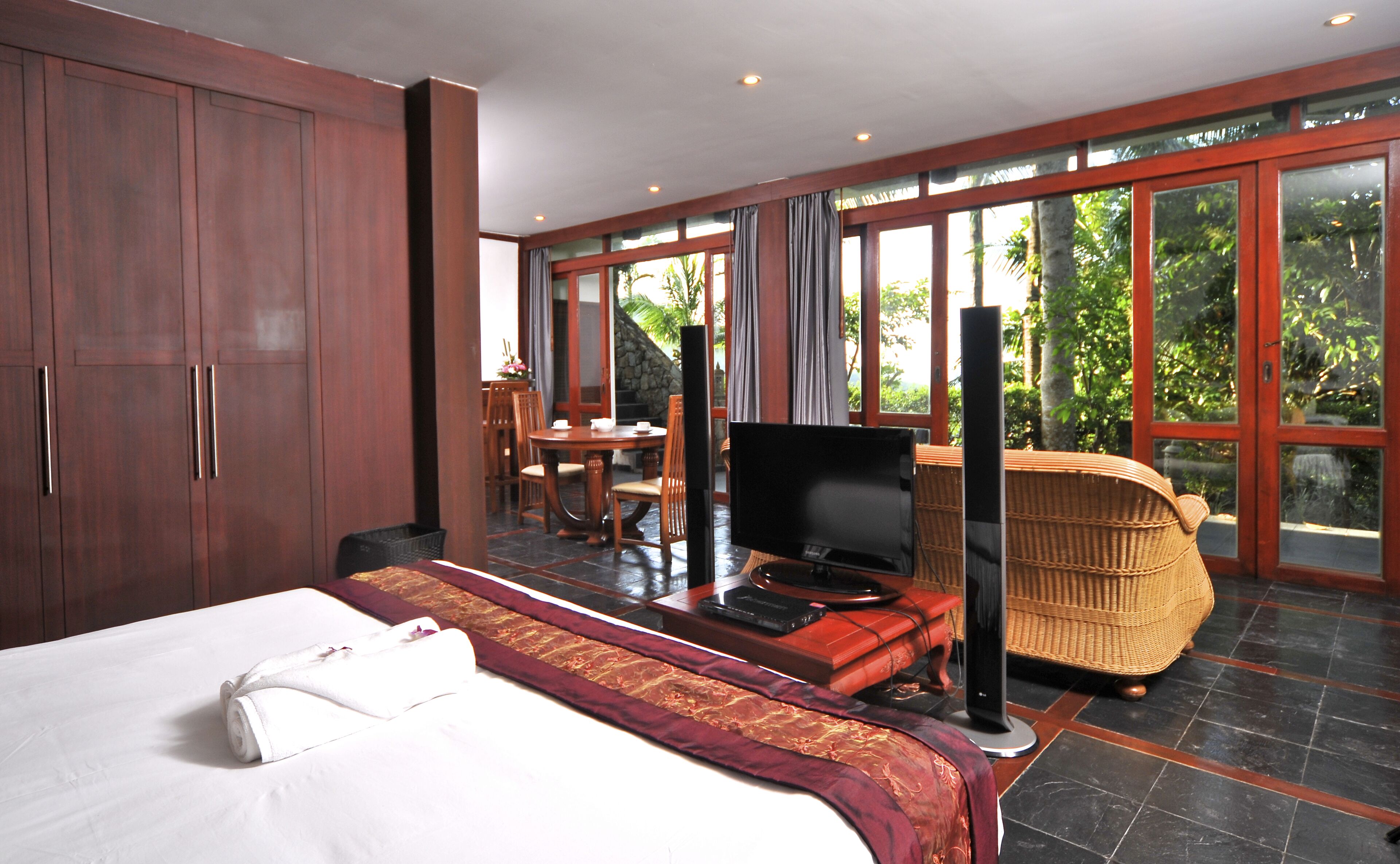 A hotel room with a bed, a television, a desk, and a wicker chair.