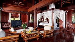 A spacious room with a large bed, a TV, and a dining area with wooden furniture.