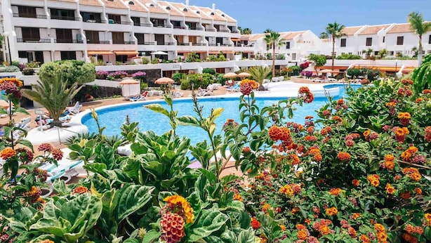 A hotel with a swimming pool surrounded by lush greenery and vibrant flowers.