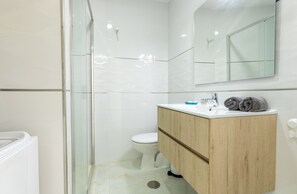 A modern bathroom with a glass shower enclosure, a white toilet, and a wooden vanity with a mirror above. - Studio Parque Santiago 1 O005 (Playa de Las Americas)