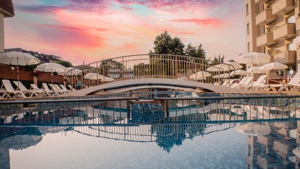 A swimming pool with lounge chairs and umbrellas, surrounded by a building with balconies. - Villa Aurora (Varna)