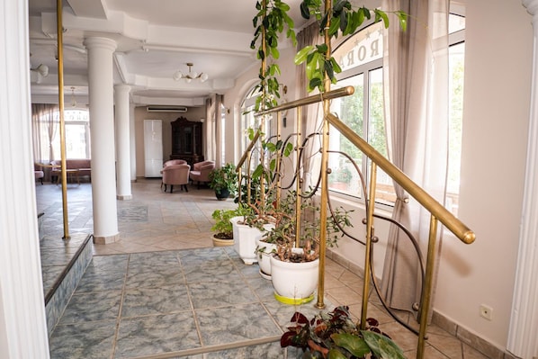 A hallway with a marble floor, potted plants, a brass railing, and a sign reading "ROOM". - Villa Aurora (Varna)