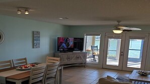 A dining area with a TV, a table with chairs, and a view of the outdoors through a glass door. - Boardwalk 201 - Serene Lake Views! Bonus Amenities include 50% off Golf Daily (Miramar Beach)