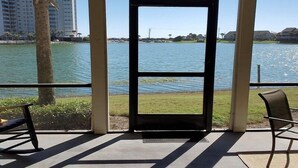 A view from a balcony with a clear lake, a palm tree, and buildings in the background. - Boardwalk 201 - Serene Lake Views! Bonus Amenities include 50% off Golf Daily (Miramar Beach)
