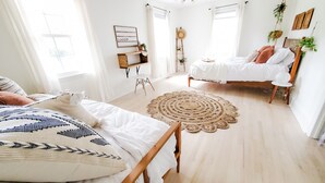 Un dormitorio luminoso y bien iluminado con dos camas, piso de madera y un tapete circular grande de tejido.