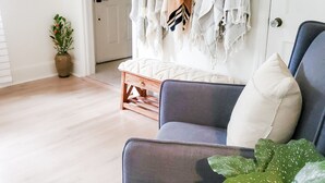Un salón con un sofá azul, una mesa de centro de madera, una planta en maceta y un perchero con varias chaquetas.