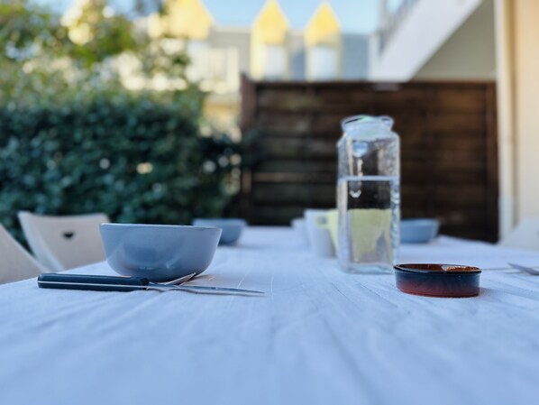 A dining table with a clear glass bottle, a bowl, and a pair of scissors. - Appartement R de C, Terrasse, Parking, Proche de la mer Dans Résidence Sécurisée (Cayeux-sur-Mer)