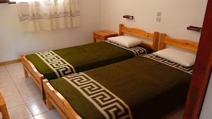 A room with two wooden beds, each with a green blanket and a white pillow. There is a small wooden nightstand beside each bed. - Anastasia Apartments (Corfu)