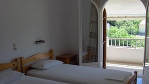A room with two wooden beds, a small wooden nightstand, and a balcony with a view of greenery. - Anastasia Apartments (Corfu)