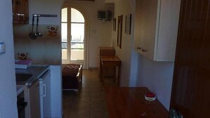 A compact kitchen with white cabinets, a wooden table, and a small TV on the wall. - Anastasia Apartments (Corfu)