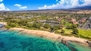Vue aérienne d’une station balnéaire avec des propriétés situées en bord de mer, un terrain de golf et, au loin, une zone résidentielle densément peuplée.