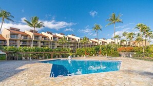 Un hôtel doté d’une piscine entourée de palmiers, avec un ciel bleu et dégagé.