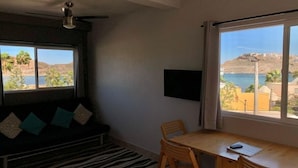 Ett rum med en soffa, ett matbord med stolar, en tv som är monterad på väggen och stora fönster med utsikt över havet och kullarna.