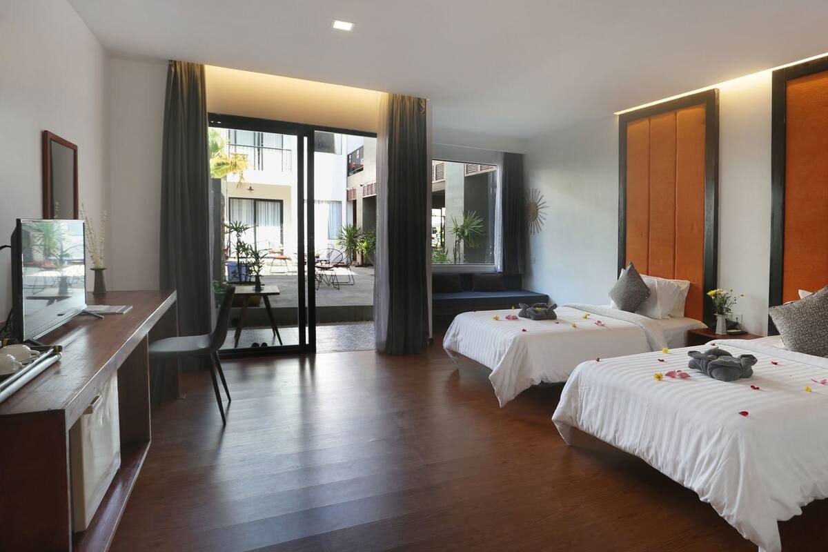 Habitación de hotel con dos camas, un escritorio, televisión y vistas al exterior.