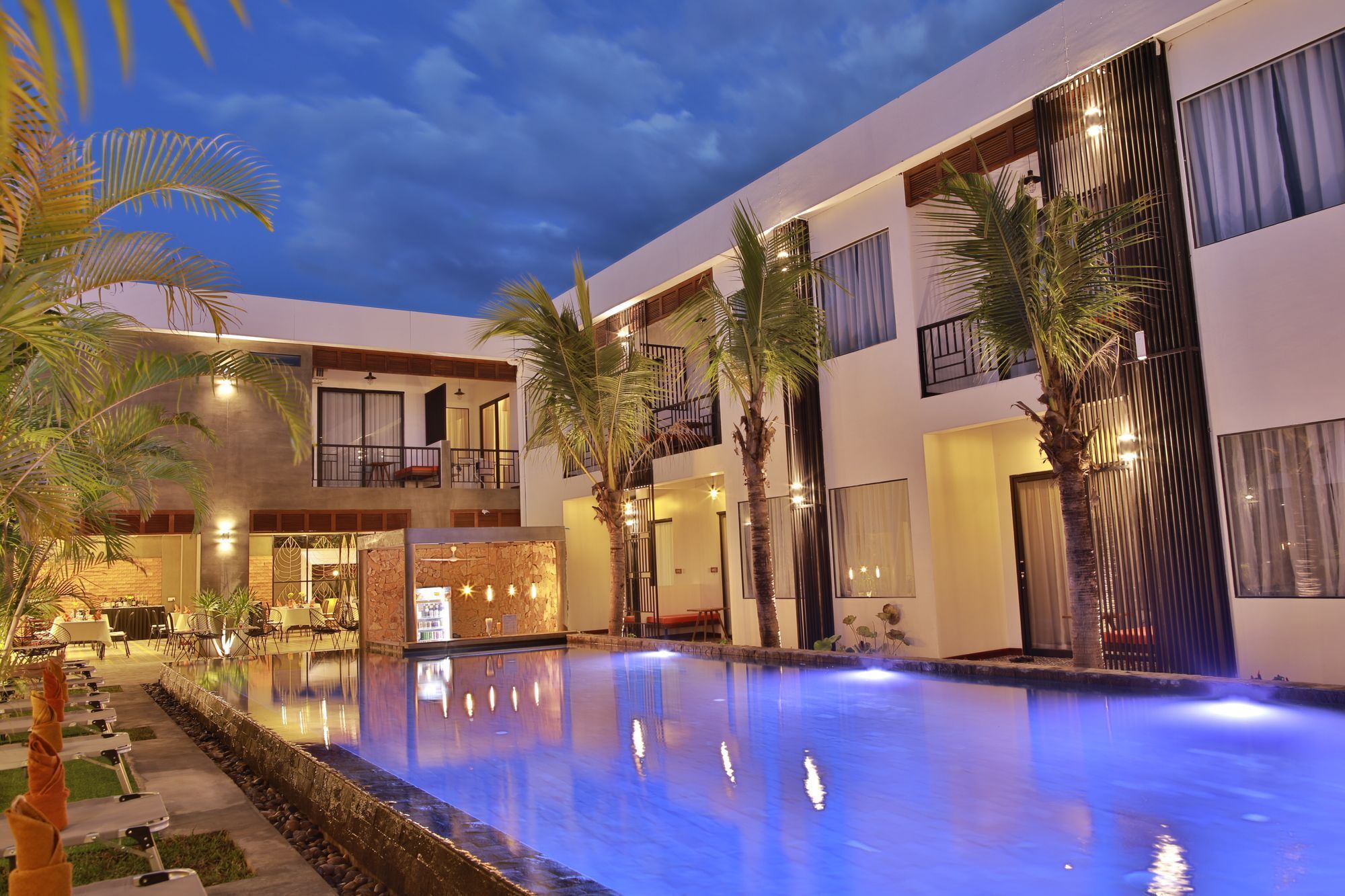 A modern hotel with a swimming pool, outdoor seating, and palm trees.