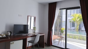 Habitación de hotel moderna con escritorio, silla, televisor y un amplio ventanal corredera que da a una zona de piscina.