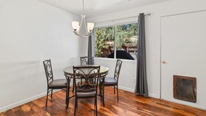 A dining area with a round table and four chairs, a chandelier, a window with curtains, and a door with a screen. - Greenlaw Getaway | 3BR | Spend Spring in Flagstaff! (Flagstaff)