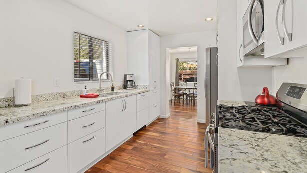 A modern kitchen with white cabinetry, a granite countertop, a stainless steel stove, and a dining area visible through an open doorway. - Greenlaw Getaway | 3BR | Spend Spring in Flagstaff! (Flagstaff)