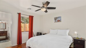 A bedroom with a bed, a nightstand, a desk, a ceiling fan, a window with curtains, a mirror, and a painting on the wall. - Greenlaw Getaway | 3BR | Spend Spring in Flagstaff! (Flagstaff)