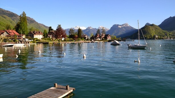 A lakeside village with boats, a wooden dock, and houses with mountain views.