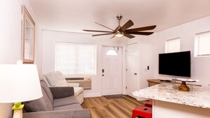 A compact living space with a ceiling fan, a flat-screen TV, a sofa, a dining area, and a kitchen counter. - Beach Condo & Pool Relaxing Getaway! Short Stride to Sandy Beach's. Unit 8 (Panama City Beach)