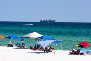 A beach with several tents and umbrellas, a large ship in the background, and people relaxing on the sand. - Beach Condo & Pool Relaxing Getaway! Short Stride to Sandy Beach's. Unit 8 (Panama City Beach)